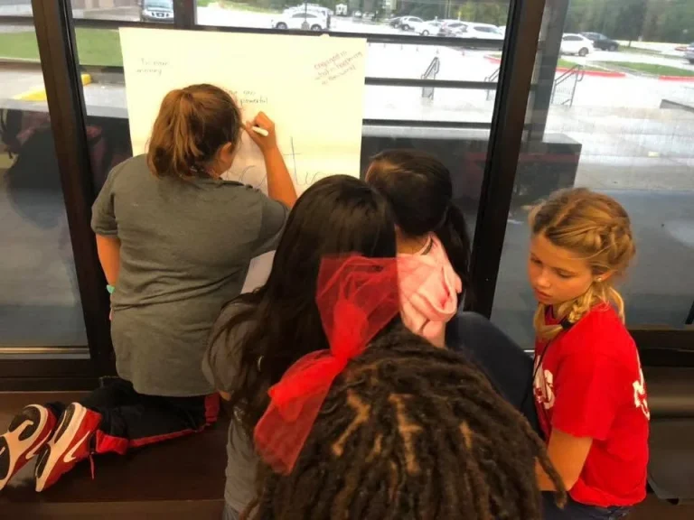 A facilitator writes on a flip chart while girls follow along